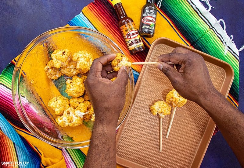 Making cauliflower lollipops Insert wood lollipop stick into cauliflower florets for spicy cauliflower recipe