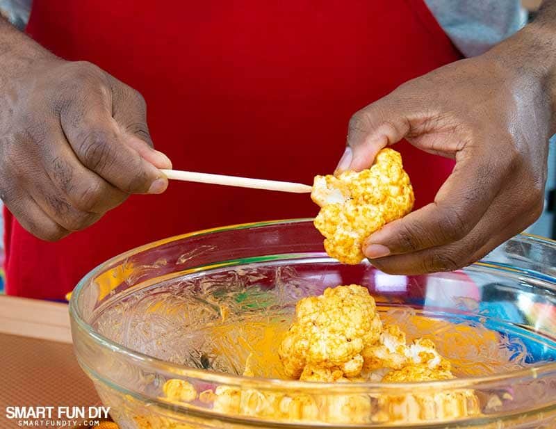 Making cauliflower florets into lollipops for spicy cauliflower recipe Front view of inserting wood lollipop stick into cauliflower florets for spicy cauliflower recipe
