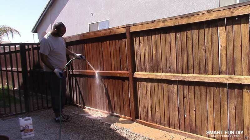 man rinsing Thompsons WaterSeal Fence Stripper from wood fence with hose