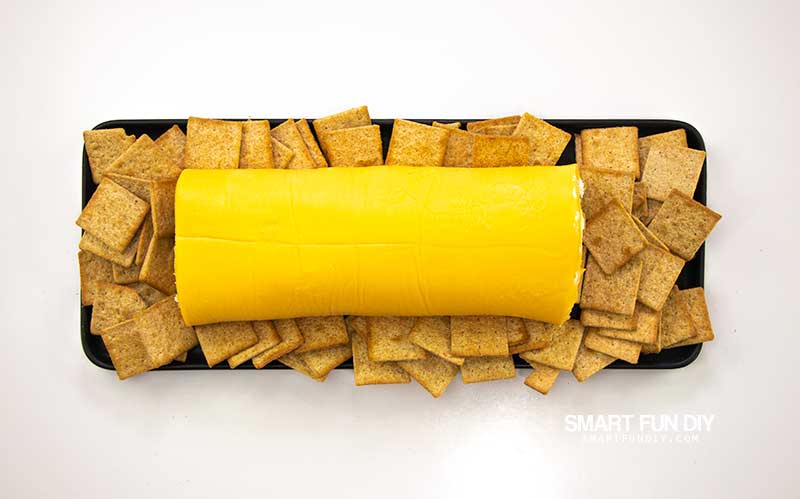 Velveeta Cheese Log on black plate surrounded by Wheat Thins crackers