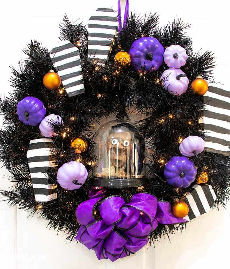 black wreath with purple punkims and black & white striped coffins on it with purple bow and shrunken Beetlejuice head inside