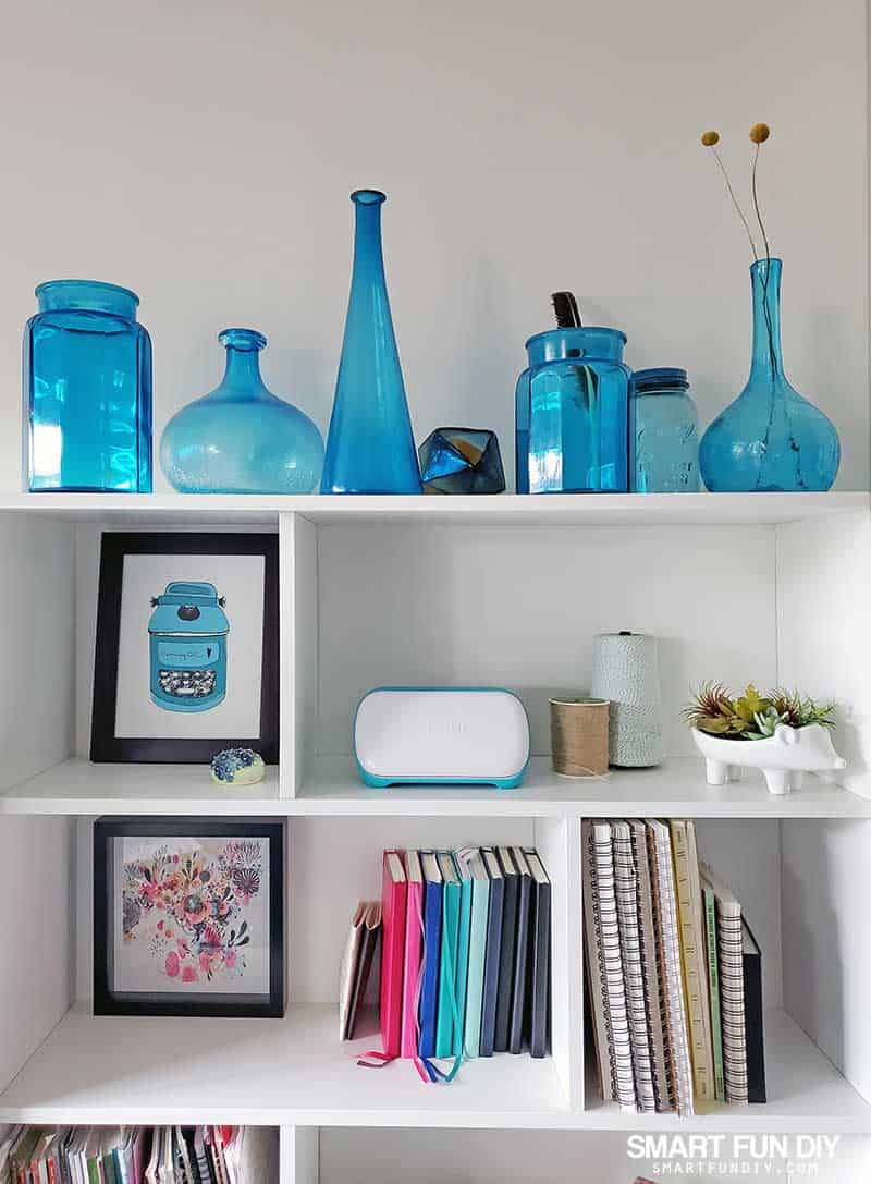 Showing Cricut Joy machine on bookshelf with home decor items, craft supplies, and books as part of a DIY lifestyle