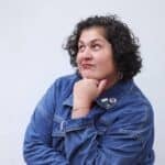 Jennifer Priest in denim jacket with fist under chin